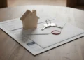 Drvena maketa kuće, ključevi i službena omotnica s dokumentima na stolu, koji simboliziraju rješavanje poreza na nekretnine i zakonska oslobođenja.
